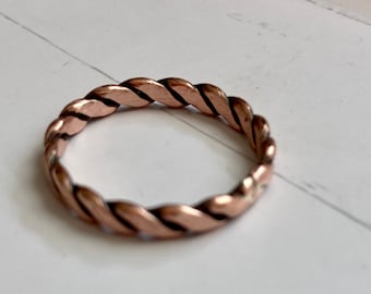 May include: A simple, twisted copper band ring. The ring is a light copper color and has a smooth, polished finish.