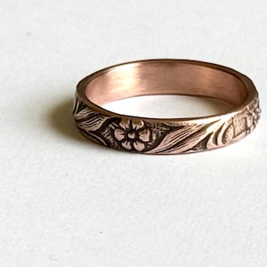 May include: A rose gold band ring with a floral design engraved around the entire band.