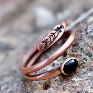 May include: A copper ring with a black onyx stone and a feather design. The ring is made of two bands of copper that are twisted together.