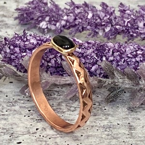 May include: A copper ring with a textured band and a black oval gemstone set in a gold bezel.