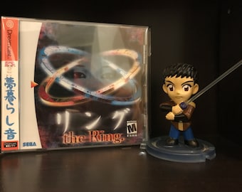 May include: A Sega Dreamcast game case for the game "The Ring" with Japanese text on the spine. The game case is next to a small plastic figurine of a character holding a sword.