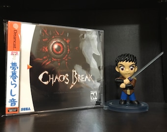 May include: A Dreamcast game case with a black and red cover featuring the text "Chaos Break" and a red eye. A small figurine of a character holding a sword is in the foreground.