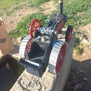 以下が含まれることがあります： 赤と黒のボイラー、赤い車輪、黒い煙突を備えた、詳細なモデルの蒸気機関。 このモデルはコンクリートの表面に置かれ、その複雑な機械的設計と構造を示しています。