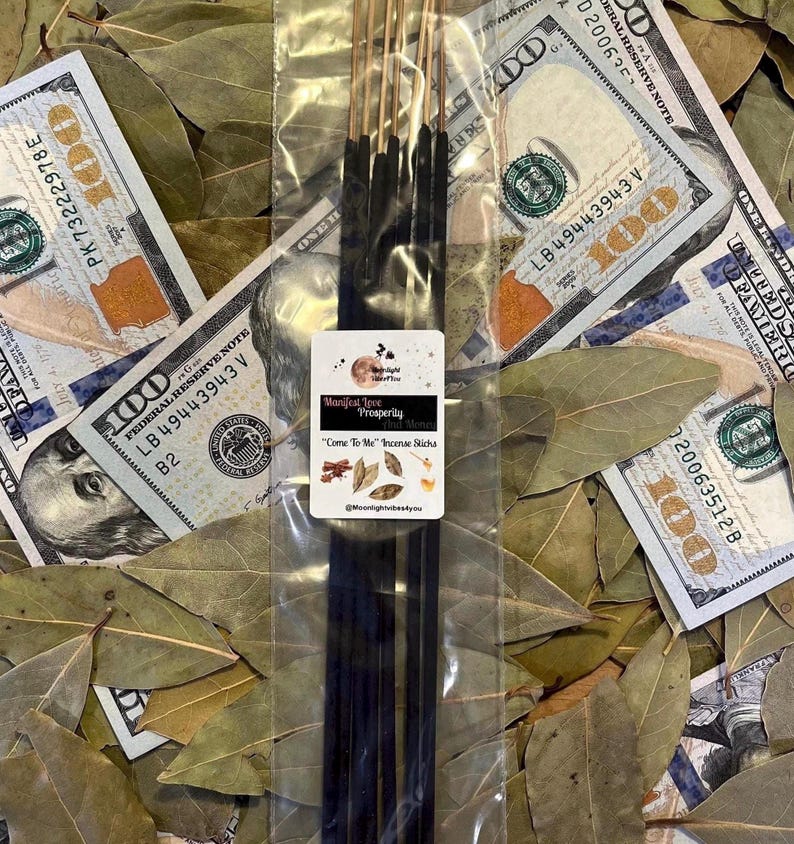 May include: A packet of incense sticks with a label reading "Manifest Love Prosperity That Money". The incense is displayed on a bed of bay leaves and surrounded by US $100 bills.