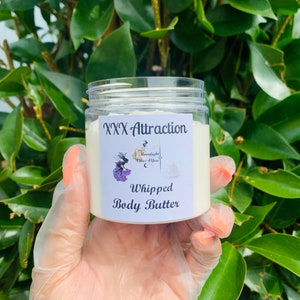 Pode incluir: Um frasco transparente de manteiga corporal batida com a etiqueta "XXX Attraction". O r&oacute;tulo apresenta um gr&aacute;fico de uma mulher e o texto "Moonlight Vibes 4 You". O frasco &eacute; segurado em uma m&atilde;o enluvada contra um fundo de folhas verdes.