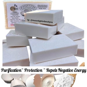 May include: A stack of white rectangular soap bars. The image includes a wrapped bar of soap with the text "Cascarilla" and "Key Ingredients" listed. The text "Purification Protection Repels Negative Energy" is also visible.