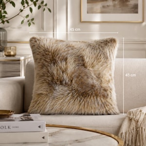May include: A square faux fur throw pillow with a variegated tan, brown, and cream color palette. The pillow features a long-pile texture and measures 18 inches by 18 inches as indicated by the dimension lines printed on the image.