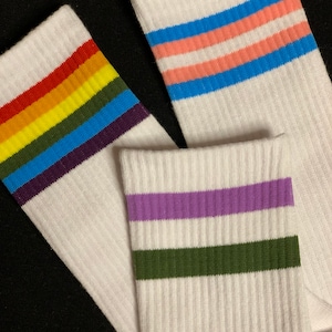 Könnte beinhalten: Drei Paar weiße Socken mit bunten Streifen. Das erste Paar hat Regenbogenstreifen, das zweite Paar hat hellblaue, rosa und hellblaue Streifen und das dritte Paar hat lila und grüne Streifen.