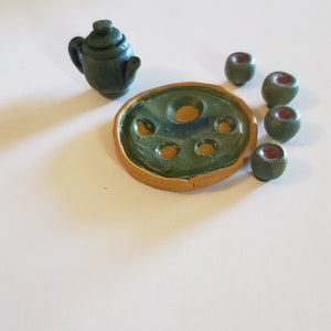 May include: A green ceramic teapot with a lid and a matching green ceramic tray with six indentations. The tray has a yellow rim.
