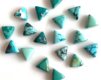 May include: A collection of turquoise triangle-shaped gemstones. The stones vary in shades of blue and green, with some displaying brown matrix patterns. The gemstones are arranged on a white surface, showcasing their polished surfaces and unique textures.