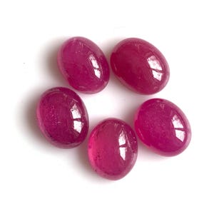 May include: Five oval-shaped, pink gemstones with a glossy finish. The gemstones are arranged in a circular pattern on a white background.