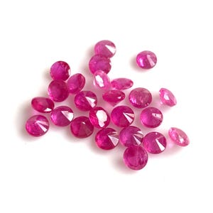 May include: A collection of round, faceted ruby gemstones in various sizes, displayed on a white background.