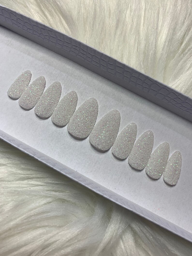 May include: A set of ten white oval-shaped press-on nails with a sparkly glitter finish.