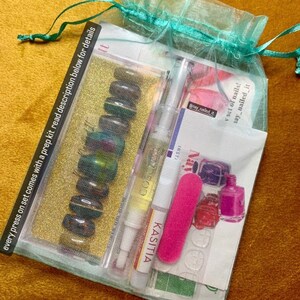 May include: A teal mesh bag filled with a set of press-on nails, a nail file, nail glue, and a bottle of nail polish. The bag has a drawstring closure and the text "may_nailed_it" is visible on one of the items.