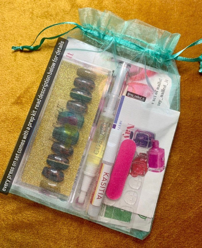 May include: A teal mesh bag filled with a set of press-on nails, a nail file, nail glue, and a bottle of nail polish. The bag has a drawstring closure and the text "may_nailed_it" is visible on one of the items.