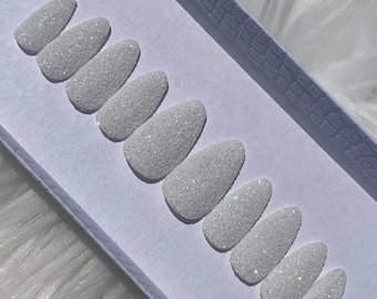 Könnte beinhalten: Ein Set mit zehn weißen, aufklebbaren Nägeln mit glitzerndem Finish. Die Nägel sind in einer Reihe auf einer weißen Oberfläche angeordnet.