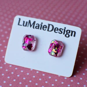 Könnte beinhalten: Ein Paar quadratische Ohrringe aus pinkfarbenem Harz mit schimmerndem Glitzer. Die Ohrringe befinden sich auf einer weißen Karte mit dem aufgedruckten Text "LuMaieDesign".