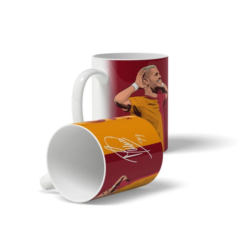 K&ouml;nnte beinhalten: Eine wei&szlig;e Keramiktasse mit einem roten und gelben Design, das einen Fu&szlig;ballspieler mit der Hand am Kopf zeigt. Die Unterschrift des Spielers steht auf der Tasse: "De Bruyne".