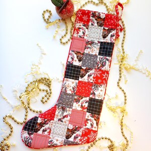 Könnte beinhalten: Ein rot-weißer Weihnachtssocken mit Patchwork-Muster, das Rentiere und Schneeflocken zeigt. Der Socken hat eine goldene Kordel und ist mit einem roten Apfel-Anhänger verziert.