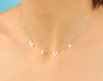 May include: A gold chain necklace with the word "MAMA" spelled out in white letters hanging from it.