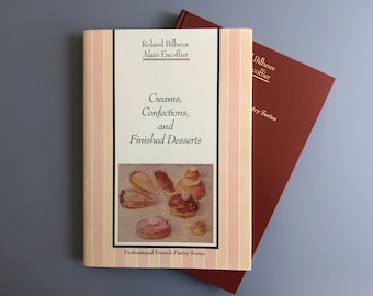 May include: Two books with a cream and peach colored cover with the title "Creams, Confections, and Finished Desserts" and the text "Professional French Pastry Series". The book cover features a painting of pastries.