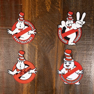 May include: Four red and white Ghostbusters patches with a no symbol and a cartoon ghost wearing a red and white striped hat. The patches say "Western Mass Ghostbusters" and "Est. 1975".