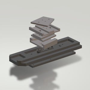 Puede incluir: Vista explosionada de un ensamblaje mecánico, renderizada en 3D. Los componentes son de varios tonos de gris, con formas rectangulares y en capas. El diseño incluye múltiples placas y piezas de conexión, lo que sugiere un sistema mecánico complejo.