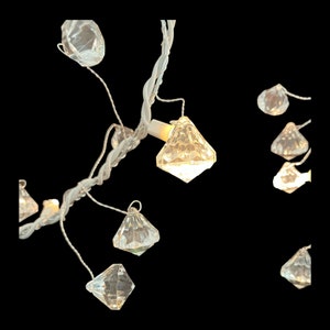 Op de afbeelding: Een string witte kerstverlichting met diamantvormige, heldere lampjes. De lampjes zijn met een dunne witte draad aan elkaar verbonden.