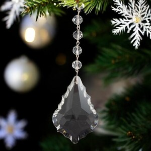 May include: A clear crystal teardrop ornament with a beaded chain hanging from a Christmas tree.