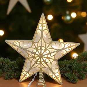 May include: A decorative Christmas tree topper in the shape of a five-pointed star. The star is gold with a filigree design and is illuminated with a warm white light. The topper sits on a gold spiral base.