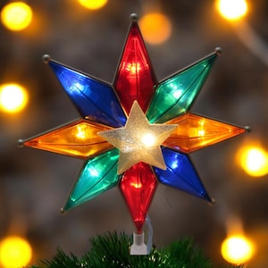 May include: A colourful, star-shaped Christmas tree topper with a gold star in the centre. The star has lights that illuminate the different coloured sections of the star.