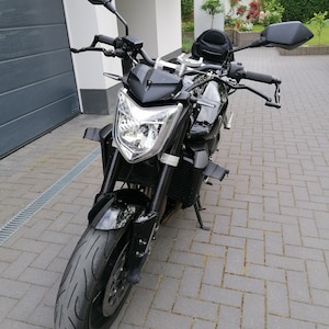 May include: A black motorcycle with a single headlight and black mirrors. The motorcycle is parked on a brick driveway.