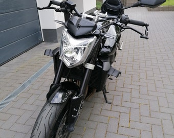 May include: A black motorcycle with a single headlight and black mirrors. The motorcycle is parked on a brick driveway.