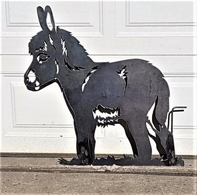 May include: Black metal silhouette of a donkey standing on a gray surface. The donkey is facing left and has a long, thin tail.