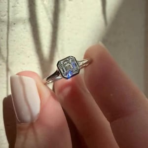 May include: A silver ring with a square-shaped diamond set in a bezel setting.