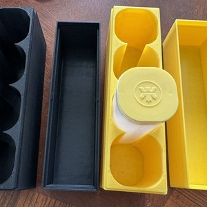 May include: Four storage containers, two black and two yellow. The black containers have three compartments each. The yellow containers have one compartment each. One of the yellow containers has a lid with a logo.