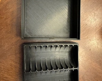 May include: A black plastic box with a removable lid. The box has a series of curved compartments inside.