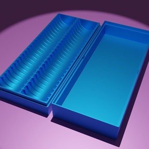 Könnte beinhalten: Eine hellblaue, rechteckige Aufbewahrungsbox mit Deckel. Das Innere der Box weist zwei Reihen gewölbter Fächer auf. Der Deckel ist geöffnet und zeigt eine glatte, flache Oberfläche. Die Box steht vor einem lila Hintergrund.