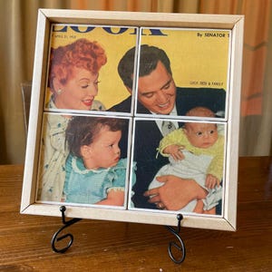 May include: A framed artwork featuring four tiles with images of Lucille Ball, Desi Arnaz, and their children. The artwork is displayed on a black metal stand. The text "LOOK" and "APRIL 21, 1953" are visible.