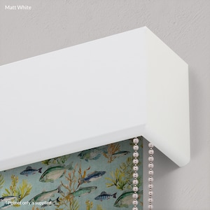 May include: A white window valance with a beaded chain pull. The valance is made of a hard, smooth material. The valance is mounted on a wall. The valance is a decorative element for a window.