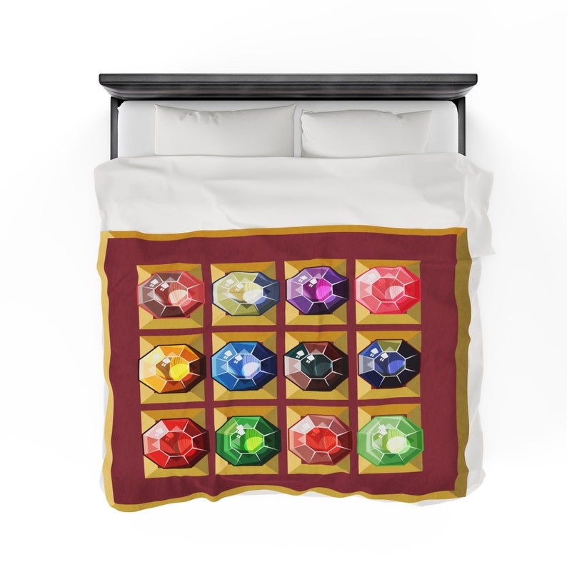 K&ouml;nnte beinhalten: Eine Bettdecke mit einem sich wiederholenden Muster aus bunten Edelsteinen. Jeder Edelstein ist in einem goldenen Quadrat auf einem weinroten Hintergrund gesetzt. Die Bettdecke liegt auf einem Bett mit wei&szlig;en Laken und Kissen.