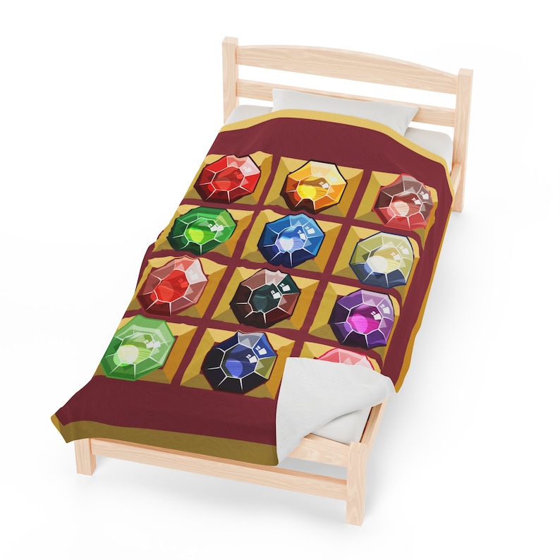 K&ouml;nnte beinhalten: Eine weinrote Decke mit einem sich wiederholenden Muster aus bunten, juwelenartigen Formen in goldenen Rahmen. Die Decke wird auf einem kleinen, hellen Holzbetttisch mit einem wei&szlig;en Kissen pr&auml;sentiert.