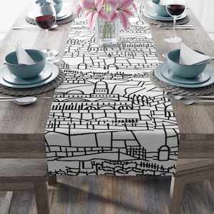 Puede incluir: Un camino de mesa blanco y negro con un diseño de horizonte de ciudad. El camino de mesa está sobre una mesa de madera con cubiertos.