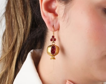 May include: Gold earrings shaped like pomegranates with red gemstone accents.