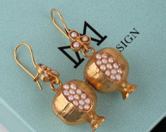 May include: Gold earrings shaped like pomegranates, each filled with white pearls. The earrings have a small flower charm with three pearls at the top of the earring.