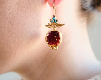 Puede incluir: Pendientes de oro en forma de granadas con piedras rojas y turquesas.