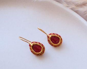 May include: A pair of gold earrings with red teardrop-shaped stones set in a detailed gold frame.