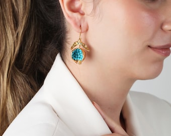 May include: Gold earrings with a turquoise pomegranate design. The earrings are dangling and have a delicate, intricate design.