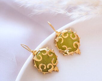 May include: A pair of gold earrings with green stone accents. The earrings feature a delicate, intricate design with a circular shape.