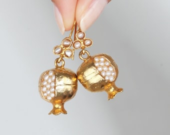 May include: Gold earrings shaped like pomegranates with white pearl accents.